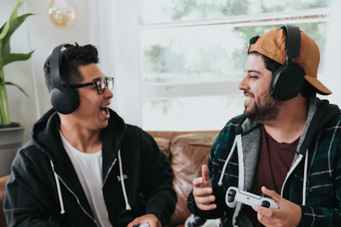 Two friends wearing headphones sitting together and gaming on a couch
